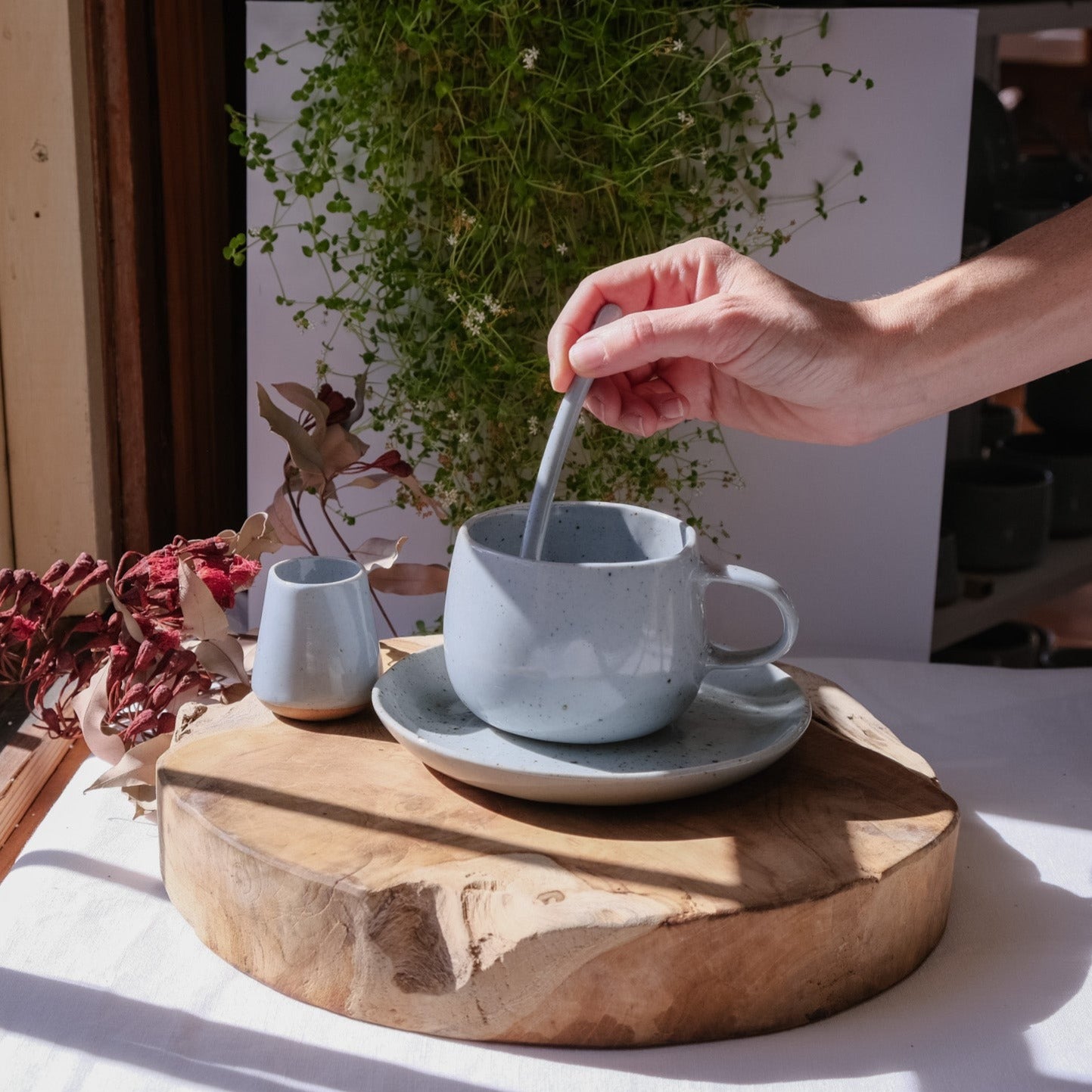 Hand stirring tea in a handmade mug, basking in the sun by Palinopsia Ceramics 