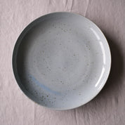 Large round serving platter by Palinopsia Ceramics in a blue and grey speckle handmade stoneware. Birdseye view on a grey tablecloth 