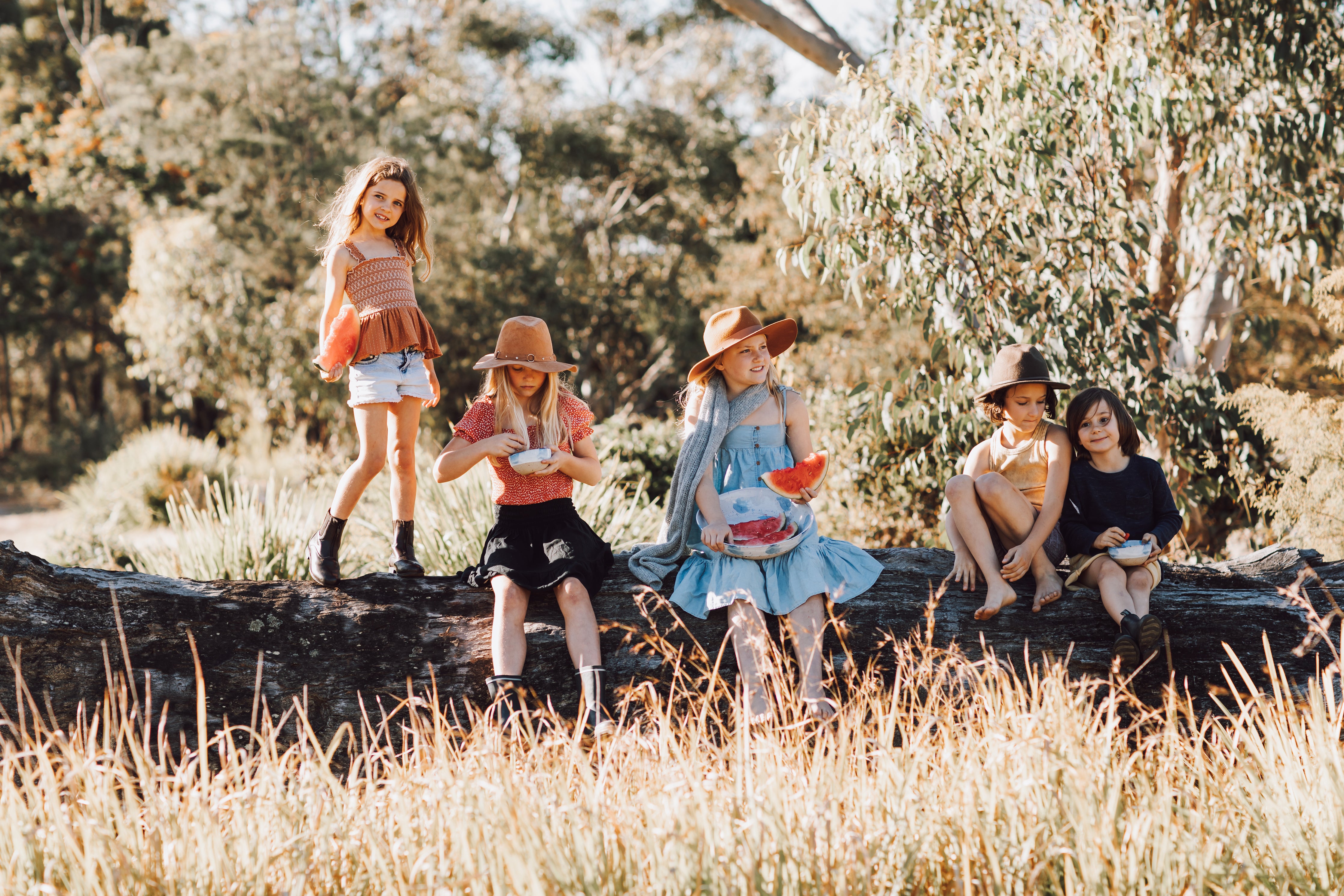 Australian Kids playing in a grassy field and sitting on a log with handmade ceramics by Palinopsia 